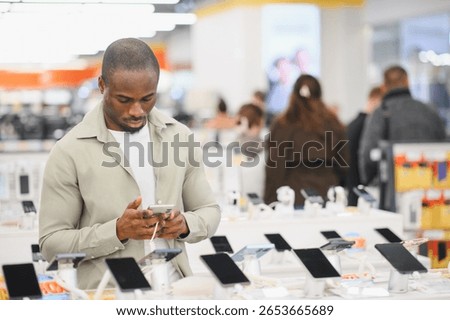 Customer comparing mobile phones using his smartphone in an electronics store, making a purchase decision