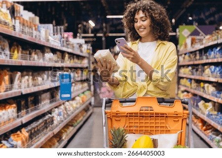 Customer comparing products information using a smartphone app while grocery shopping in a supermarket