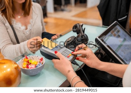Customer completing a transaction by tapping a credit card on a payment terminal, while a cashier assists, symbolizing modern retail experiences and secure commerce technology