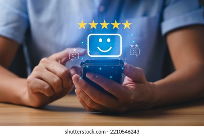 Customer and Consumer Satisfaction Concept. Businessmen or customers express their satisfaction through an application on a smartphone screen to choose  5 star rating and smiley face emoji - Powered by Shutterstock