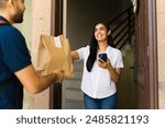 Customer delighted to receive a food delivery at home from a delivery person using a smartphone app