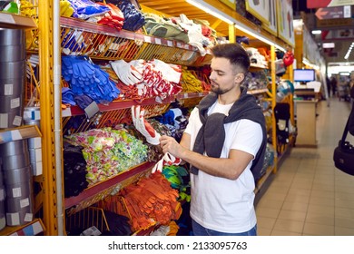 Customer at DIY store choosing a pair of rubber gloves. Young man standing near shelf with different rubber working gloves and putting one pair on to see if they fit. Shopping for DIY goods concept
