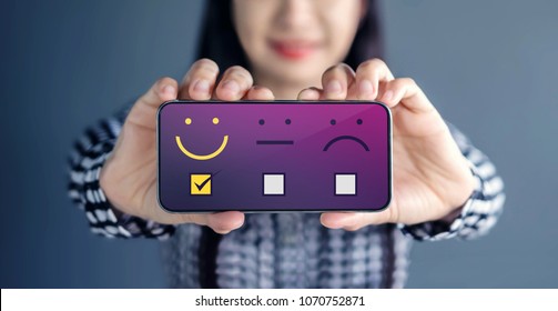 Customer Experience Concept. Happy Woman Show Her Satisfaction On Smart Phone With A Checked Box On Excellent Smiley Face Rating