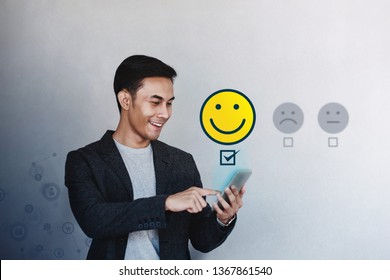 Customer Experience Concept. Young Businessman Giving His Positive Review In Satisfaction Online Survey. Happy Client Submit A Smiling Face For Excellent Services Via Smartphone