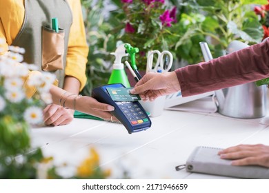 Customer at the florist shop, she is paying with her credit card, the shop owner is holding the POS terminal, hands close up - Powered by Shutterstock