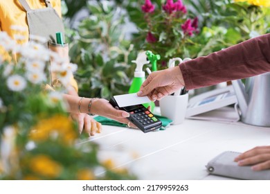 Customer at the florist shop, she is paying with her credit card, the shop owner is holding the POS terminal, hands close up - Powered by Shutterstock