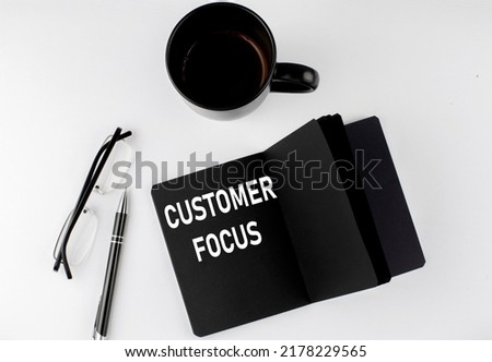 CUSTOMER FOCUS written text in small black notebook with coffee , pen and glasess on a white background. Black-white style