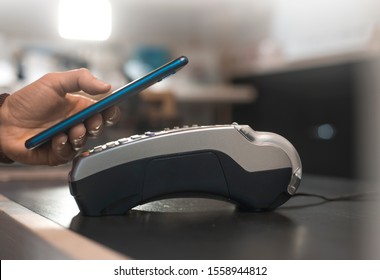 Customer Hand Pays With Smartphone In Store Using NFC Technology. Mobile Phone Paying The Bill With Contact Less Technology.