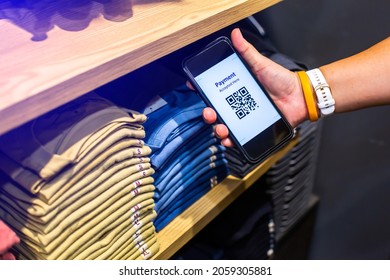 Customer Hand Using Smart Phone To Scan QR Code Tag With Many Row Of Clothes  To Accepted Generate Digital Pay Without Money. Qr Code Payment Concept.