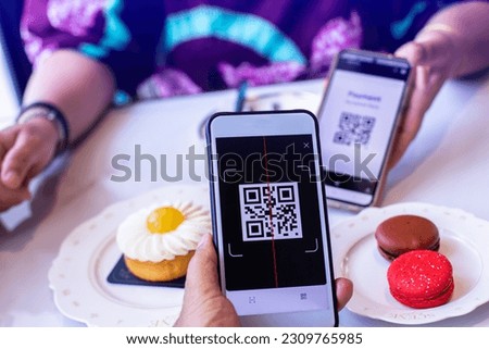 Customer hand using smart phone to scan QR code tag with blur  colourful macaroons cakes of different colors in coffee shop or restaurant to accepted generate digital pay without money. Qr code paymen