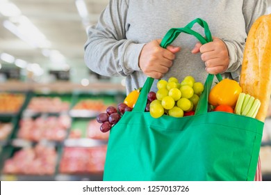 Customer hold reusable green shopping bag with fruit and vegetable over Supermarket aisle blur defocused product shelves interior bokeh light background