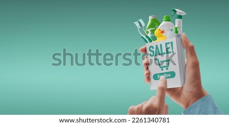 Customer holding a miniature shopping bag and ordering detergents online, she is pressing the buy now button