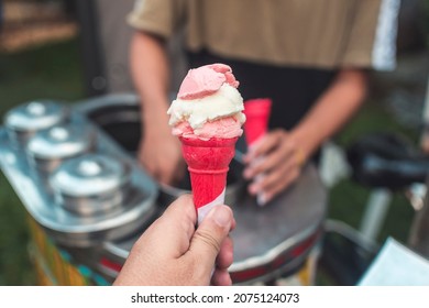 A customer holding pink wafer cone filled with scoops of coconut and strawberry sorbetes. Traditional ice cream in the Philippines.
