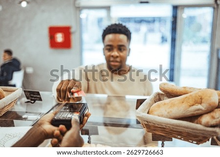 A customer makes a payment using a credit card over a bakery counter featuring fresh bread. Illustrates contactless payment methods and modern purchasing transactions in a bakery business setting.
