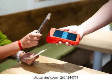Customer making contactless payment using nfc technology on smartphone in a restaurant, holding the phone close to the pos terminal