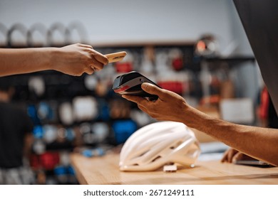 Customer making a contactless payment using NFC technology on a smartphone in a bike shop, holding it near the POS terminal