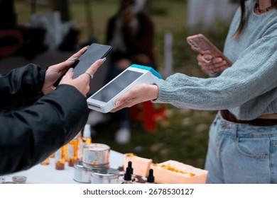 Customer making a contactless payment using nfc technology on a mobile pos terminal held by a vendor at an outdoor market