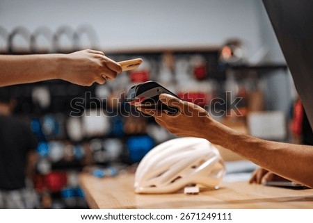 Customer making a contactless payment using NFC technology on a smartphone in a bike shop, holding it near the POS terminal