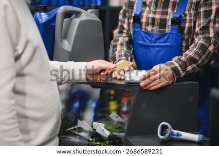 Customer making a contactless payment using credit card at a car parts store, assisted by the salesman
