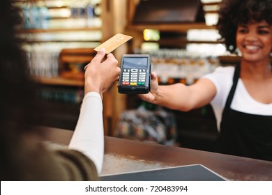 Customer making wireless or contactless payment using credit card. Smiling cashier accepting payment over nfc technology.
