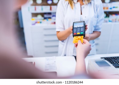 Customer Paying Bill By Credit Card.  Woman Purchasing Medical Products. Paying With Credit Card In Drugstore. Pharmacist Holding Security Device For Customer In Drug Store