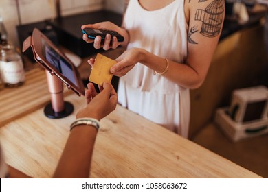 Customer Paying The Bill Using A Credit Card At A Cafe. Woman Entrepreneur Holding A Wireless Point Of Sale Machine To Effect Card Transaction.