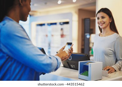 Customer Paying For Order With Phone And Pin Pad In Front Of Cheerful Cashier Sales Woman At Store