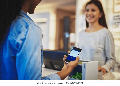 Customer Paying With Phone And Pin Pad In Front Of Smiling Cashier Salesperson At Store