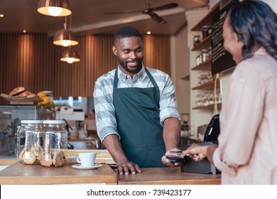 Customer paying a smiling barista for a purchase in a cafe using a smartphone and nfs technology  - Powered by Shutterstock