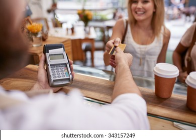 Customer paying for their order with a credit card in a cafe. Bartender holding a credit card reader machine and returning the debit card to female customer after payments.
