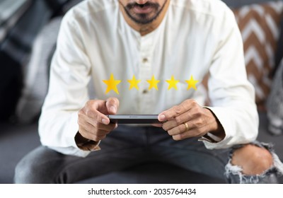 Customer Pressing On Smartphone With Five Stars Icon For Feedback Review Satisfaction Service While Sitting On Sofa In Living Room At Home