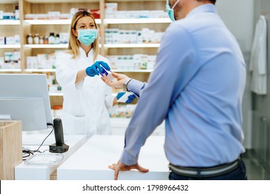 Customer With Protective Mask On His Face Buying Pills In Modern Drugstore.  