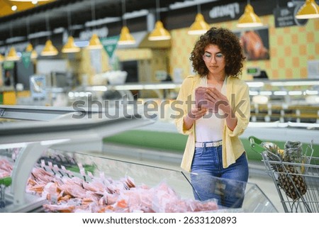 Customer reading label of packaged ham, shopping for groceries in supermarket refrigerated aisle
