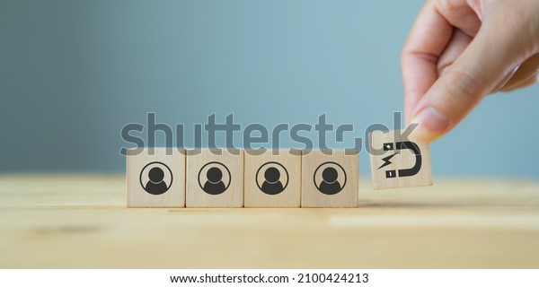 Customer retention concept. Inbound marketing\
strategy. Attracting potential customers.  Hand puts wooden cubes\
with magnet attracts customer icons on beautiful grey background\
and copy space.\
Loyalty