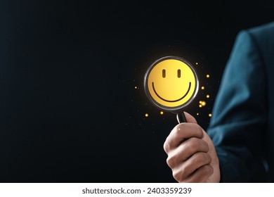 Customer Satisfaction Survey concept, businessman holding magnifying glass focus to smiley face emoticon for service experience rating online application. Good feedback rating.