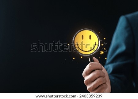 Customer Satisfaction Survey concept, businessman holding magnifying glass focus to smiley face emoticon for service experience rating online application. Good feedback rating.