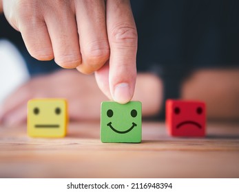 Customer satisfaction survey concept. Close up customer hand choose happy smiley face, blurred neutral and sad face icon on wood cube to survey feedback, rating, review, service satisfaction.