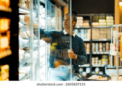 Cliente seleccionando comestibles de la sección refrigerada en un supermercado, sosteniendo el Carrito de compras