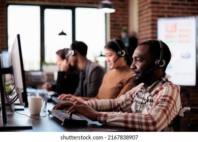 Customer service employee with chronic health condition working at call center helpdesk. Male client care operator with impairment sitting in wheelchair in disability friendly office.