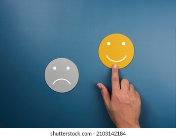 Customer service evaluation, ratings, feedback, client experience, satisfaction survey concepts. Happy smile on yellow face chosen by customer's hand near sad face on blue background, minimal style.