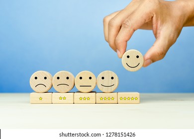 Customer service evaluation and satisfaction survey concepts. The client's hand picked the happy face smile face icon and five star symbol on wooden cube on table