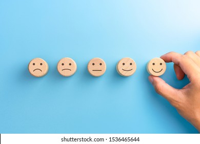 Customer Service Evaluation And Satisfaction Survey Concepts. The Client's Hand Picked The Happy Face Smile Face Icon On Wooden Cube On Blue Background. Copy Space