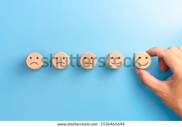 Customer service evaluation and\
satisfaction survey concepts. The client\'s hand picked the happy\
face smile face icon on wooden cube on blue background. copy\
space