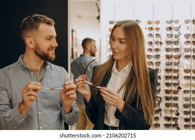 Customer shoosing spectacles at optic store with the lelp of sales person