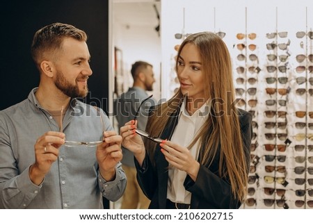 Customer shoosing spectacles at optic store with the lelp of sales person