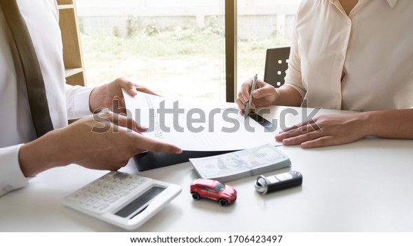 Customer is signing the car rental agreement and\
getting a car key from dealer after signed in the office, Car\
rental concept.