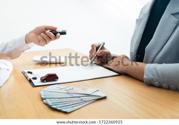 Customer is signing the car rental agreement and\
getting a car key from dealer after signed in the office, Car\
rental concept.