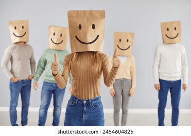 Customer with smiley bag on head feels happy, leaves positive review, gives thumbs up. Portrait of casual woman in shopping bag with cheerful face emoticon in studio with group of people in background - Powered by Shutterstock