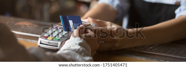 Customer stand near bar counter make payment use\
contactless credit card close up hands device view, cashless method\
pay bills in commercial places concept. Horizontal banner for\
website header design