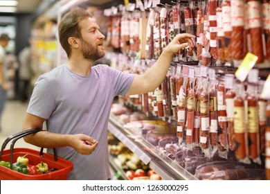 Customer standing in meat section and choosing salami or sausages. Bearded man holding basket and looking at meat assortment. Concept of buying food in supermarket and gastronomy. - Powered by Shutterstock